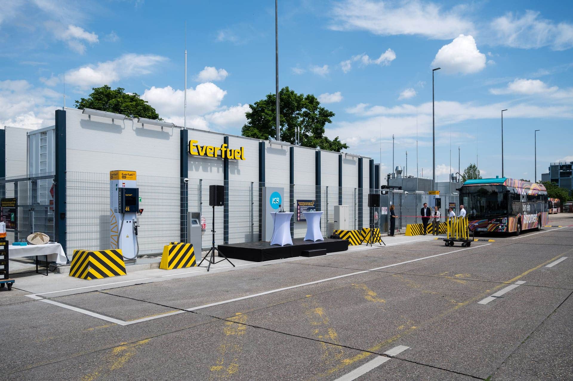 Gesamtanlage der Wasserstofftankstelle mit Menschen und einem Bus im Hintergrund