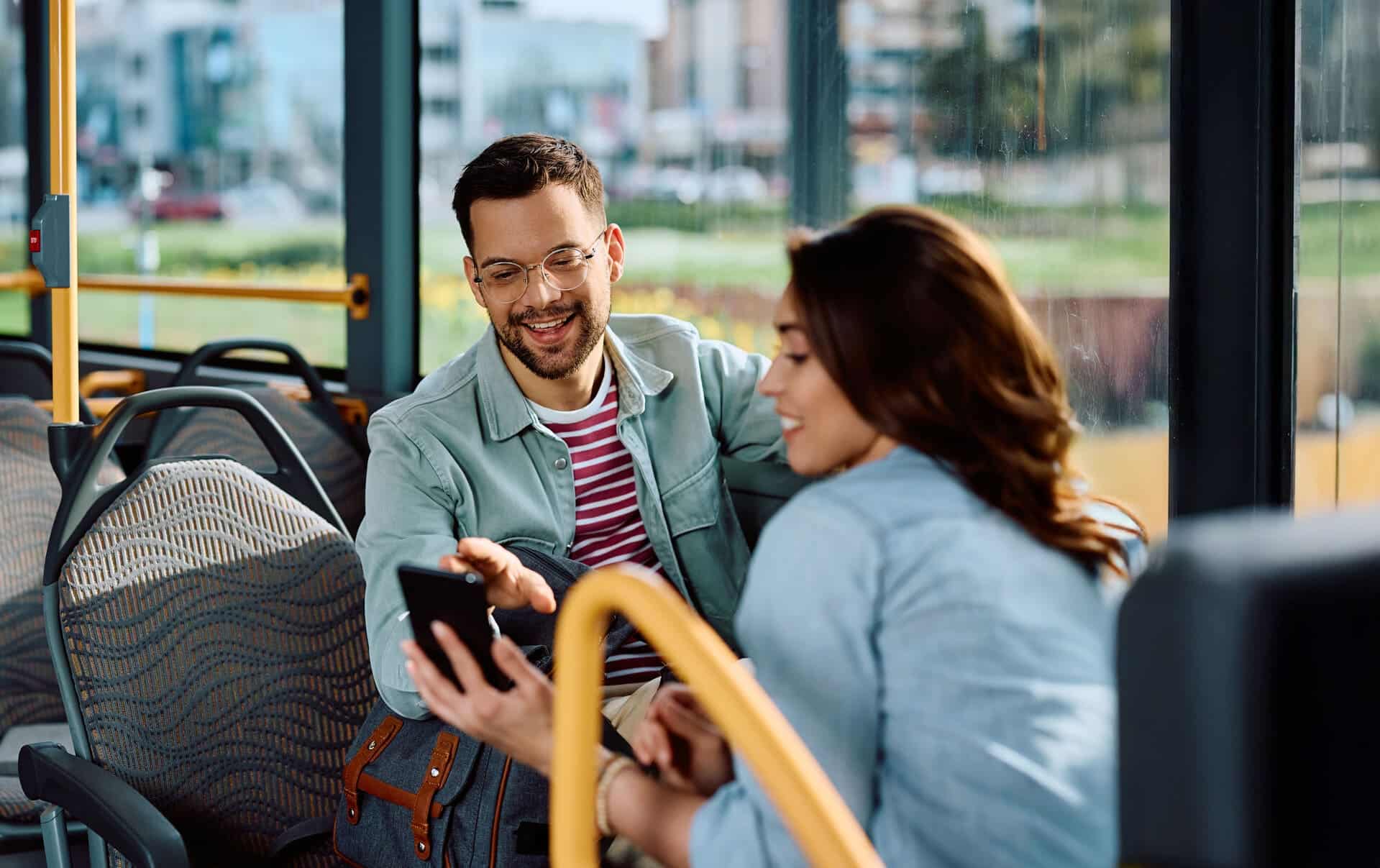 Mann und Frau sitzen im Bus und schauen gemeinsam auf ein Smartphone